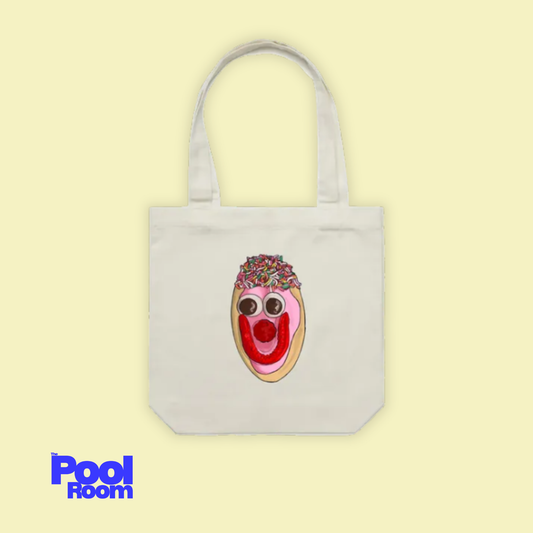 A light yellow background with a cream coloured cotton tote bag featuring a hand-drawn illustration of an Australian pink-iced Smiley Bikkie by The Pool Room.